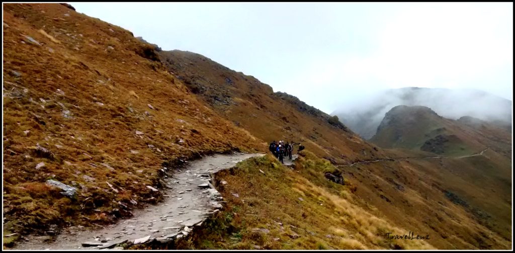 Trekkers walk across a mountain path from Ali Bugyal to Pathar Nachauni