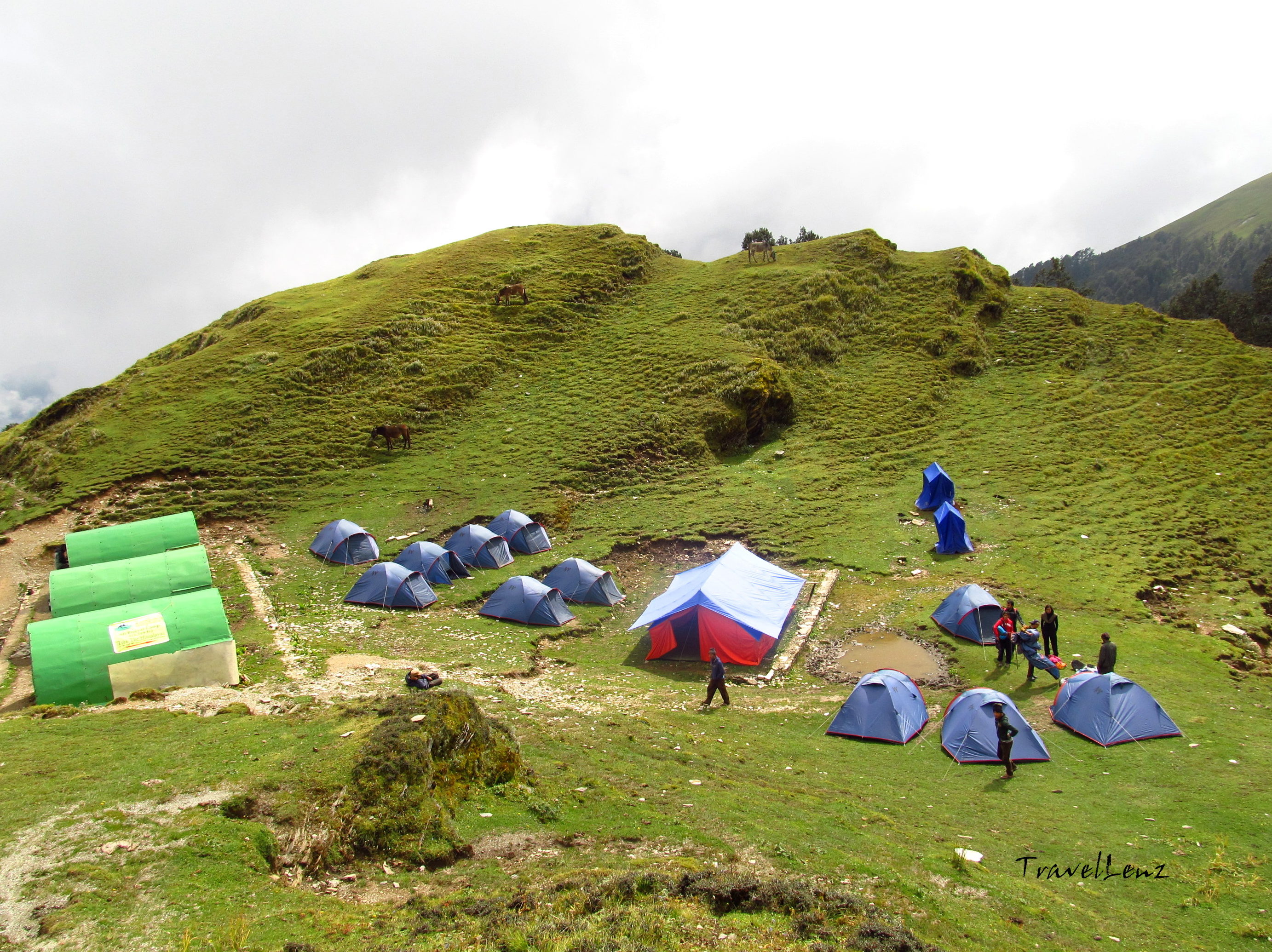 A campsite on a grassland comprising of a dozen of blue tents, three fibreglass tents and a mess tent.