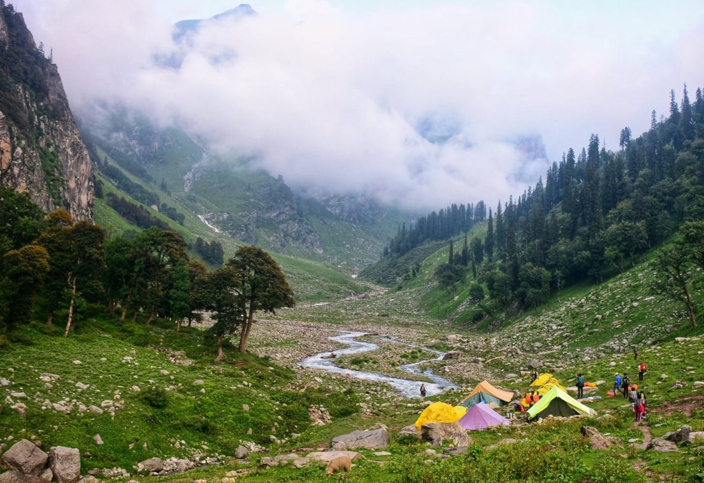 Mountain valley with a trekking tents in a campsite in green meadows under a cloudy sky