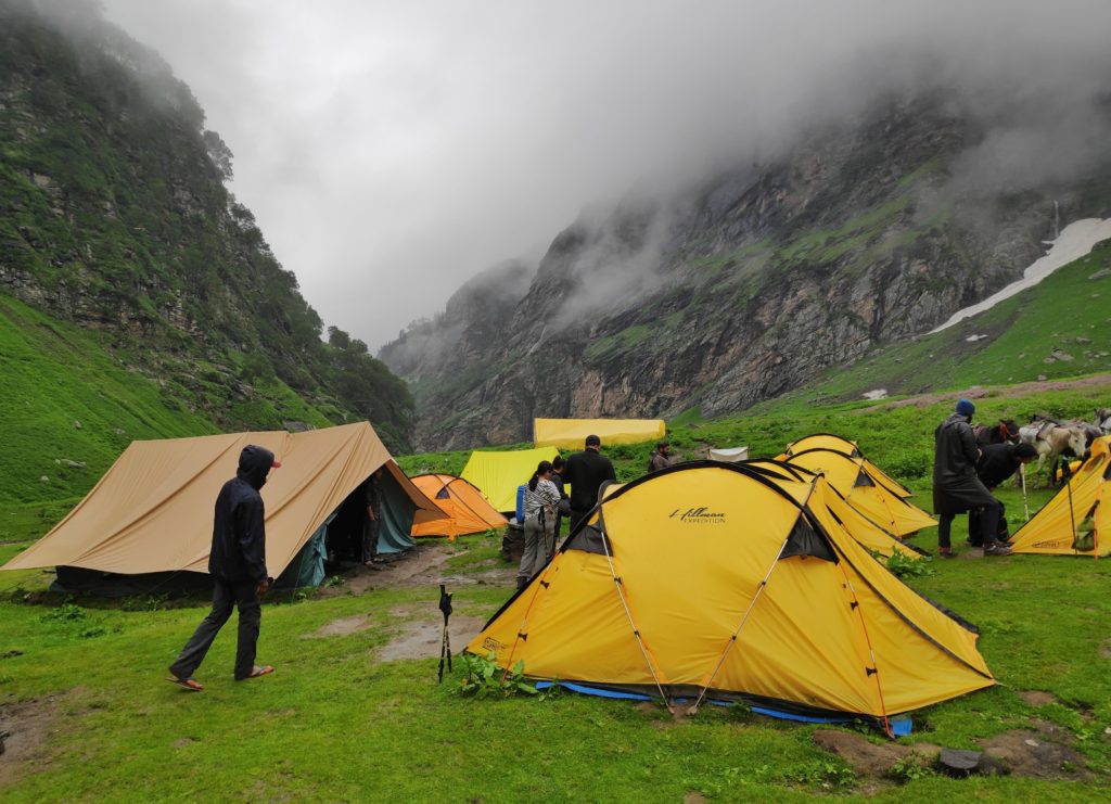 Misty mountain meadow with yellow tents and people around it