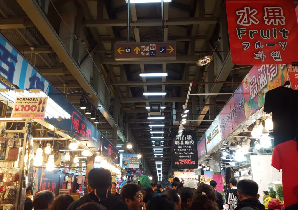Night market with brightly lit shops in front of busy street with many shoppers