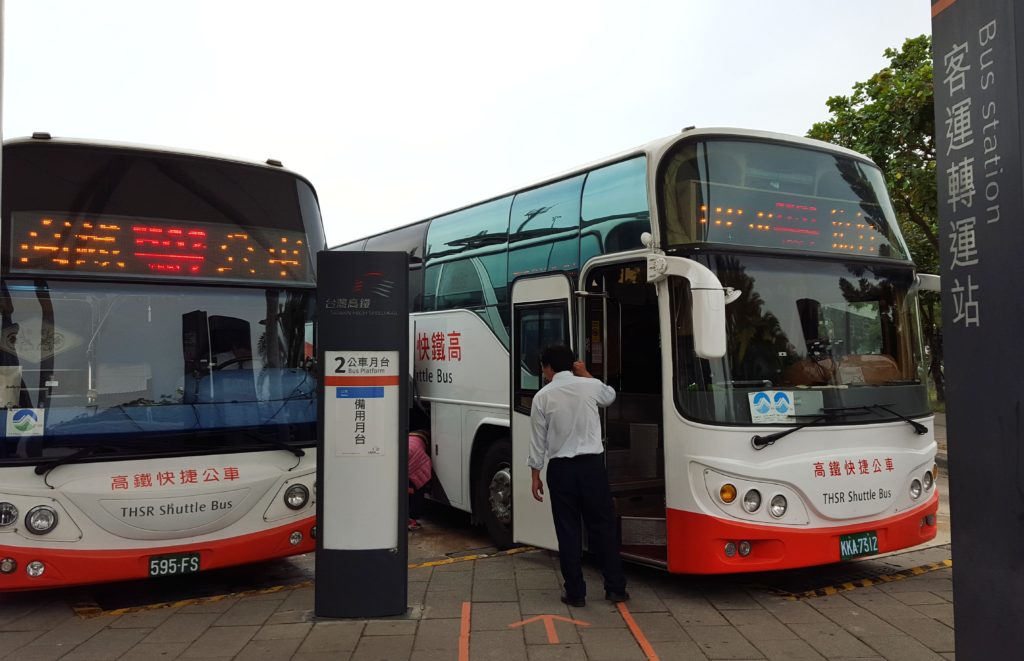 Two buses at a bus station with passengers boarding.