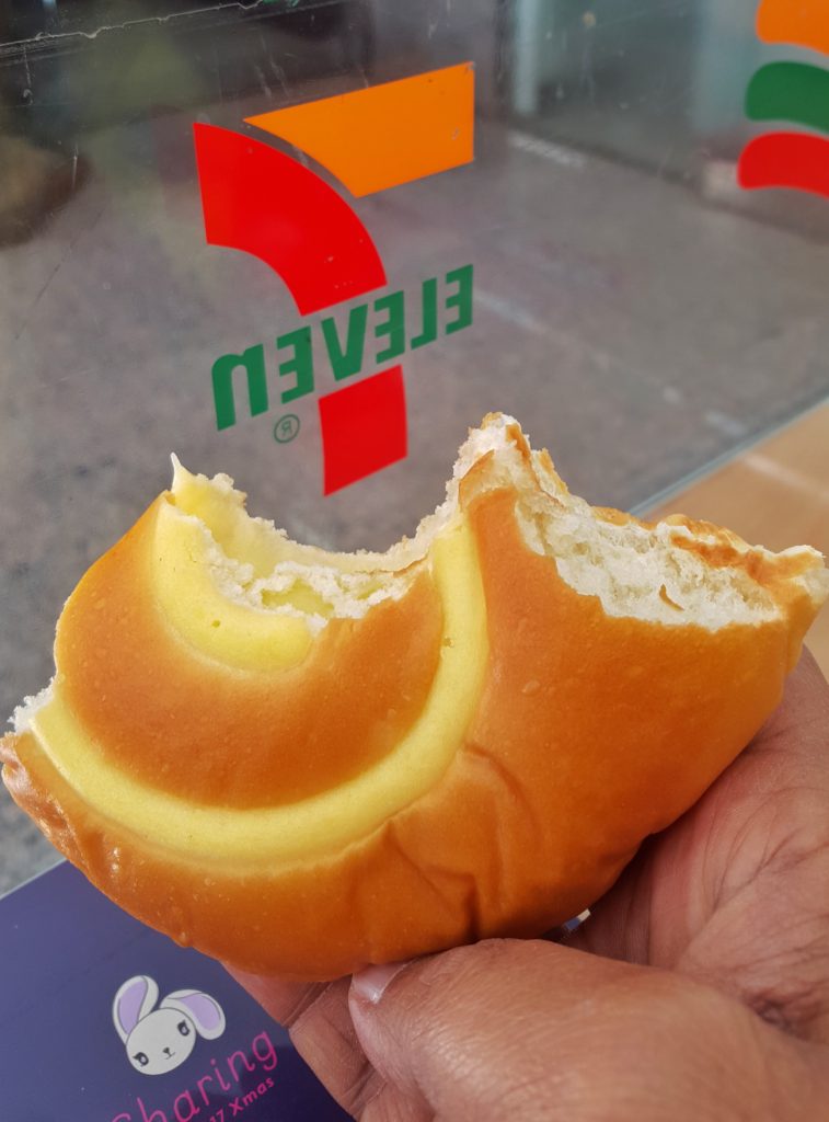 A hand holding a cream bun in front of a sign in a shop