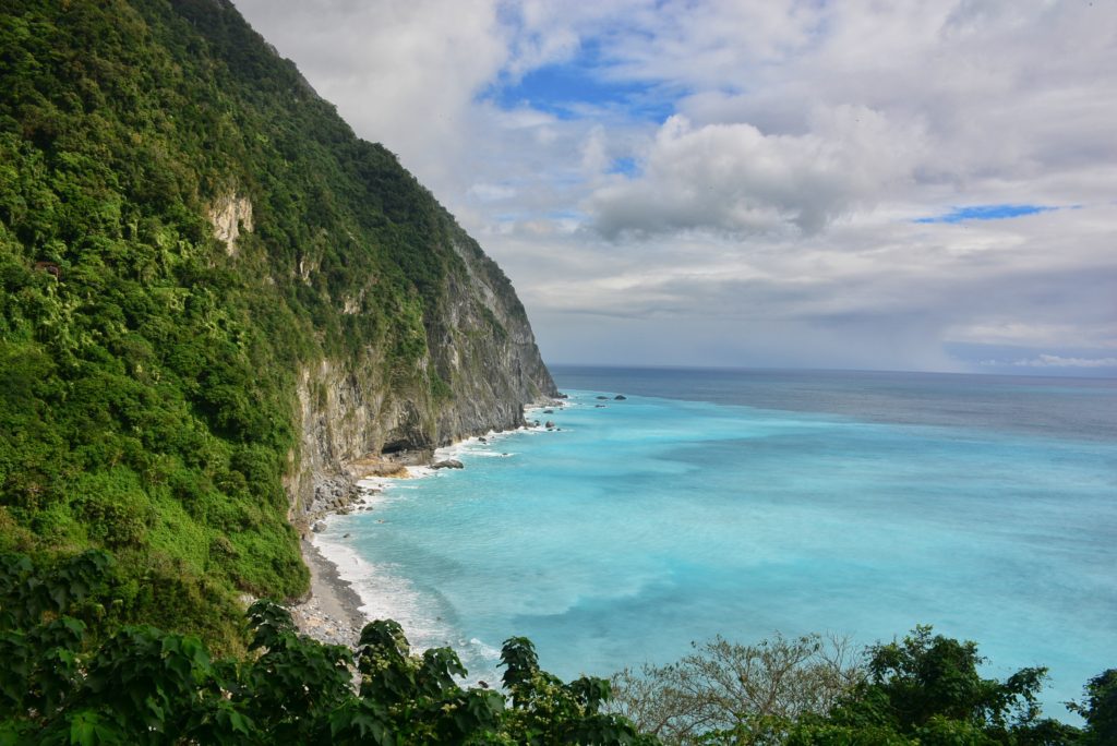 Turquoise blue green sea with a beach and cliffs with clouds in a blue sky