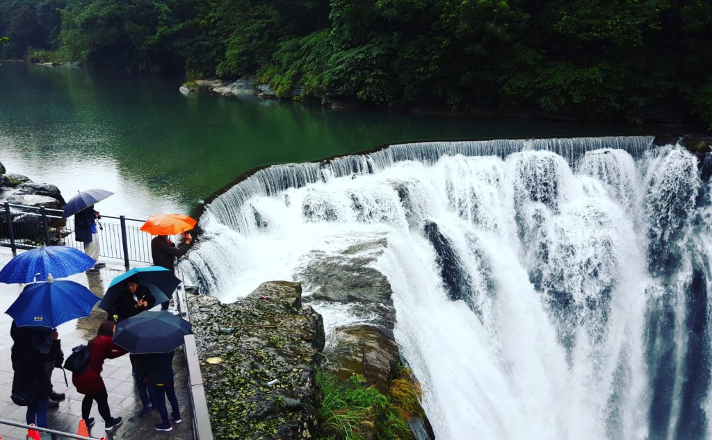 Gushing waterfall with people holding umbrellas standing and watching