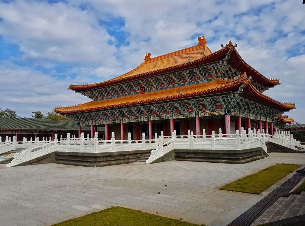 A big red and white temple in a big compound under a cloudy blue sky