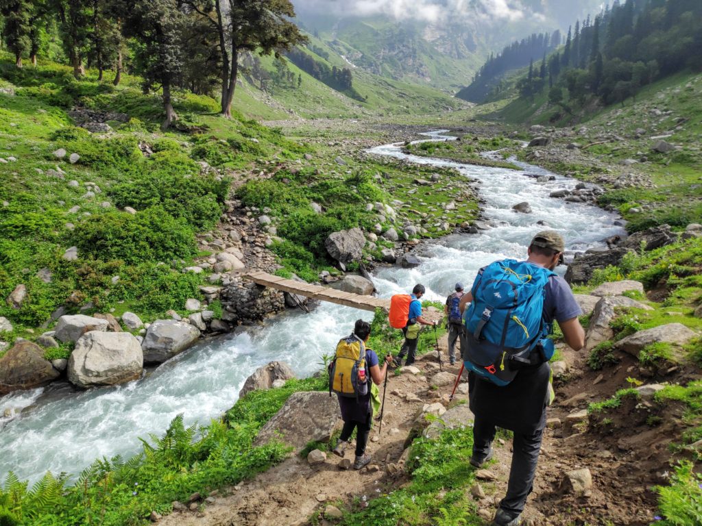 Trekkers hiking to cross a wooden bridge on a river in a hilly meadow