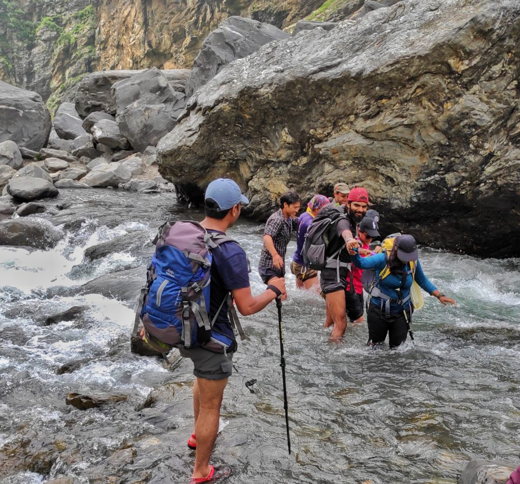 Trekkers crossing a stream with trek leader and the group walking in a file