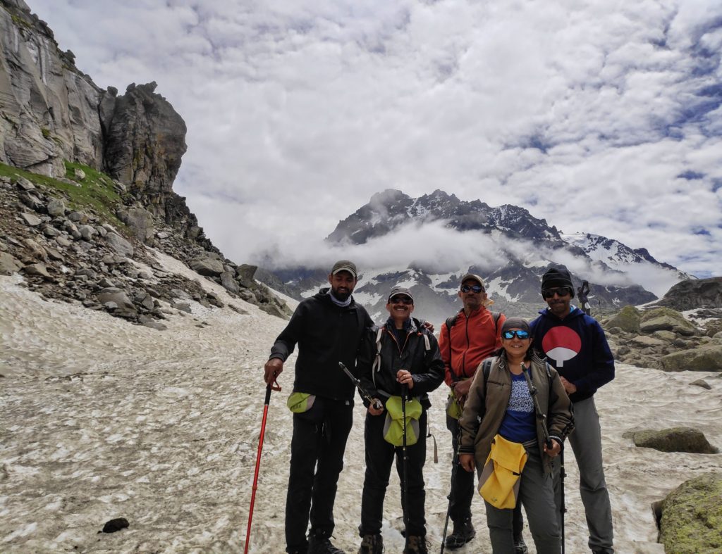 5 trekkers standing on the snow covered mountains with peaks behind them under cloudy skies