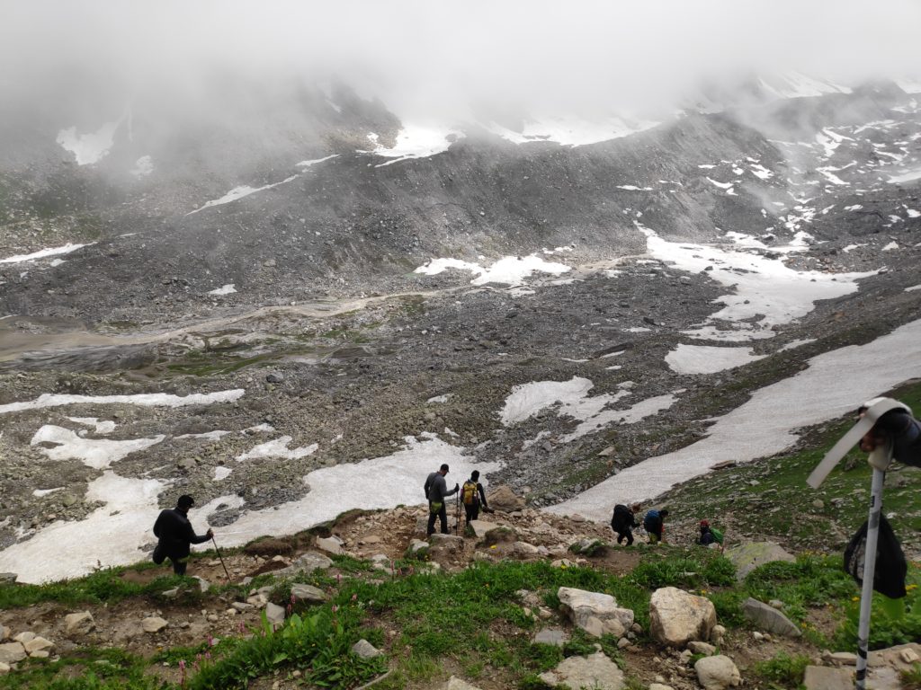 Trekkers descending a mountain path to a rocky valley with snow in places