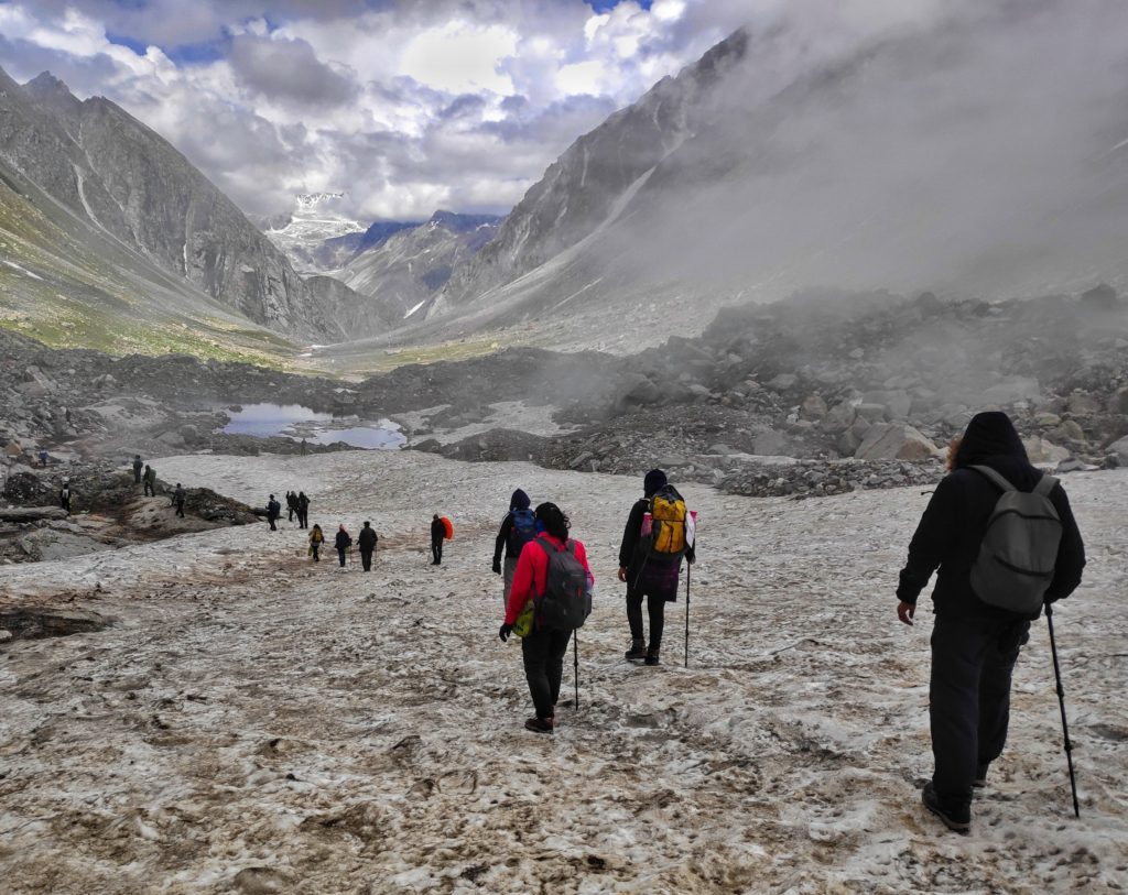 Trekkers walking along a snow clad valley surrounded by barren rocky mountains