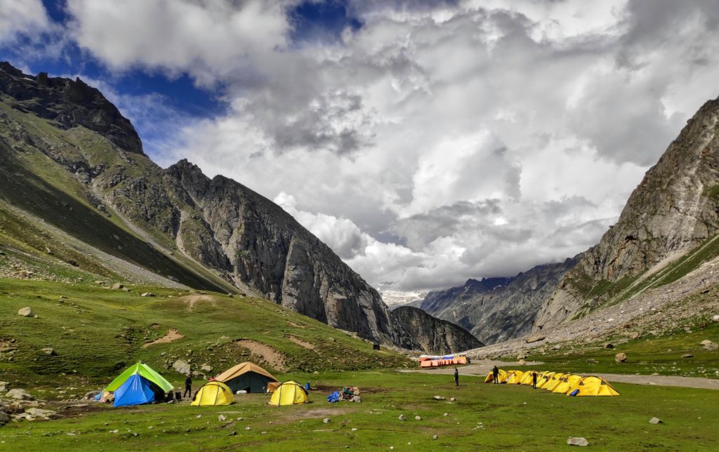 Mountain valley with clouds above and a meadow with yellow tents pitched