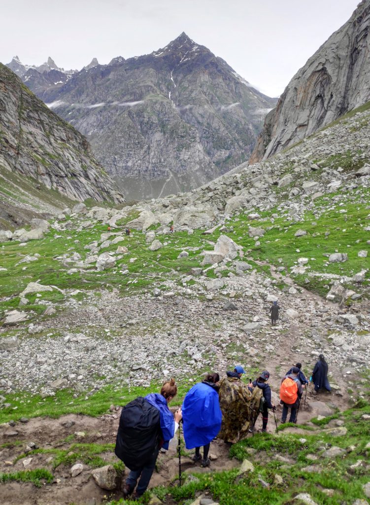 Trekkers descending into a rocky and barren valley with sparse vegetation