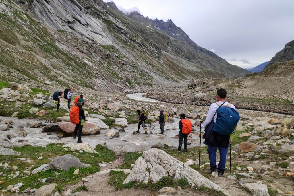Trekkers crossing a stream with rocks in a barren mountain valley