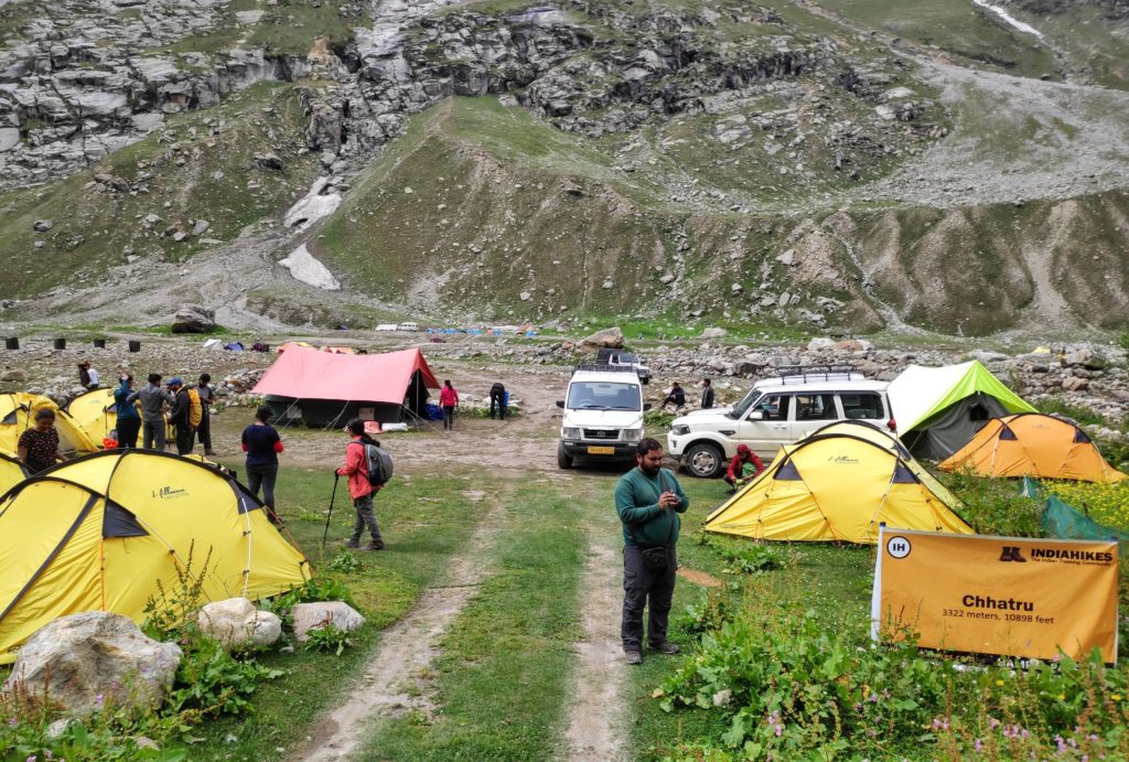 A hilly and rocky setting with yellow tents and vehicles with people around