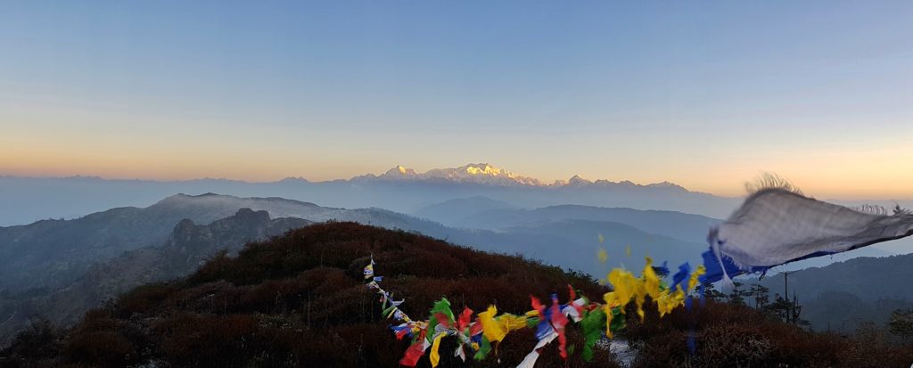 Sunrise over a snow capped mountain range with blue sky and a string of colourful prayer flags in the foreground